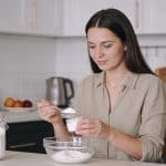 Femme assise cuisine mesurant sucre blanc avec cuillere