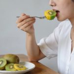 Femme assise a table mangeant kiwi jaune et vert