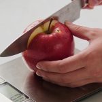 Nutritionniste tranchant une pomme rouge sur balance